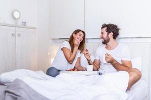 Young handsome man feeding attractive young woman in bed in the morning. Romantic breakfast for two. Love , care, relatioships. couple having healthy breakfast together in bed at home photo