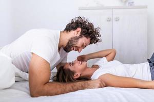 cariñosa joven pareja atractiva compartiendo un momento romántico en el dormitorio en casa. feliz pareja joven abrazándose y sonriendo mientras está acostado en la cama en un dormitorio en casa. foto