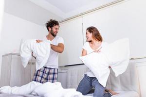 Happy young couple is having fun in bed. Enjoying the company of each other. Pillow battle Funny couple fighting with pillows in bed photo