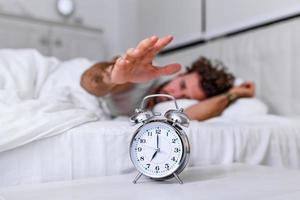 Man lying in bed turning off an alarm clock in the morning at 7am. Hand turns off the alarm clock waking up at morning, man turns off the alarm clock waking up in the morning from a call. photo