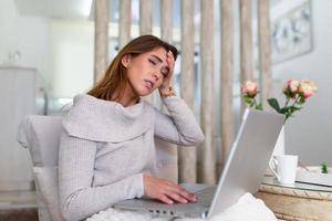 Feeling exhausted. Frustrated young woman looking exhausted while sitting at her working place at home. Freelance overworked having headache photo