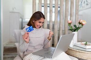 mujer joven en el sofá de compras en línea con tarjeta de débito. hermosa chica usando una computadora portátil para comprar en línea en casa. hermosa chica usando una computadora portátil para comprar en línea en casa foto