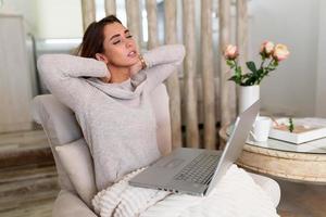 mujer de negocios siente dolor en el cuello después de sentarse en la mesa con una computadora portátil. mujer cansada que sufre del síndrome de la oficina debido a largas horas de trabajo en la computadora. linda chica masajeando sus tensos músculos del cuello foto