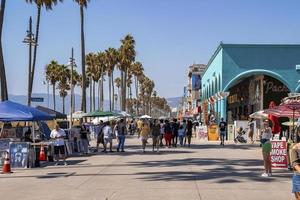 Tourists walking on boardwalk by palm trees and buildings at Venice beach photo