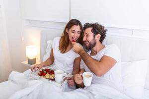 pareja enamorada desayunando en la cama. joven pareja caucásica desayunando romántico en la cama. hembra y macho, dos tazas de café, frutas y galletas coloridas. foto