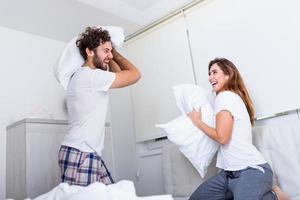 Couple having a fun while pillow fight. Young happy couple beat the pillows on the bed in a bedroom at home. photo