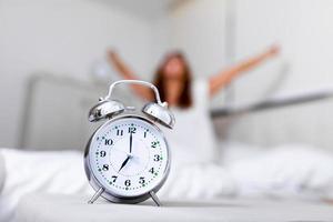 reloj despertador de primer plano que tiene un buen día con antecedentes mujer feliz estirándose en la cama después de despertarse, luz del sol por la mañana. despertarse por la mañana a tiempo foto