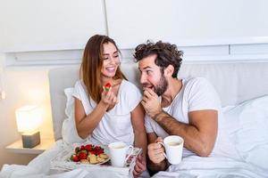 joven pareja casada enamorada desayunando en su cama. buenos días desayuno saludable en la cama. joven y hermosa pareja de amor está desayunando en la cama. foto