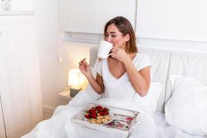 Woman having breakfast and cup of coffee in the hotel room . Tray with breakfast on a bed for lovely beautiful girl. Beautiful woman laying and enjoying, breakfast in bed photo