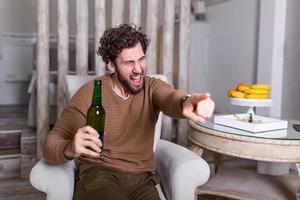 Excited sports fan sitting in an sofa and watching a match on television. leisure, sport, entertainment and people concept - man watching football or soccer game on tv at home and drinking beer photo