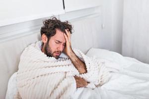 hombre enfermo con gripe acostado en la cama controlando su temperatura y bebiendo bebidas calientes. hombre enfermo acostado en la cama con fiebre alta. gripe fría y migraña. foto