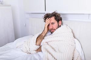 Sick man with seasonal infections, flu, allergy lying in bed. Sick handsome man covered with a blanket lying in bed with high fever and a flu, resting. photo