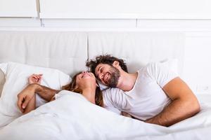 Happy couple is lying in bed together. Enjoying the company of each other.Happy young couple hugging and smiling while lying on the bed in a bedroom at home. photo