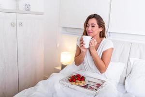 Woman having breakfast and cup of coffee in the hotel room . Tray with breakfast on a bed for lovely beautiful girl. Beautiful woman laying and enjoying, breakfast in bed photo