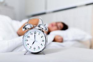 Wake up of an asleep girl stopping alarm clock on the bed in the morning. woman sleeping and wake up to turn off the alarm clock in the morning photo