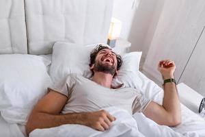 joven durmiendo despertándose y estirándose en su cama. gente, hora de acostarse y concepto de descanso - hombre acostado en la cama en casa, es hora de despertar foto