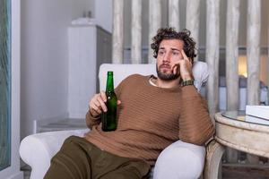 Triste fanático de los deportes sentado en un sofá y viendo un partido en la televisión con su equipo perdiendo el juego. hombre viendo fútbol o fútbol en la televisión en casa y bebiendo cerveza foto