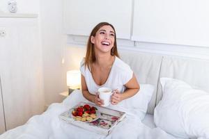 Breakfast in bed for young beautiful woman. Woman having breakfast in bed with fruits, coffee and biscuits. Morning waking up in hotel photo