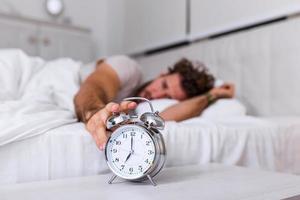 Man lying in bed turning off an alarm clock in the morning at 7am. Hand turns off the alarm clock waking up at morning, man turns off the alarm clock waking up in the morning from a call. photo