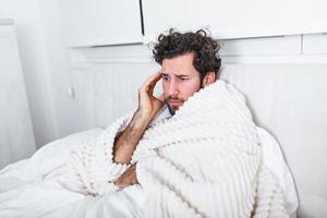 Sick man with seasonal infections, flu, allergy lying in bed. Sick handsome man covered with a blanket lying in bed with high fever and a flu, resting. photo