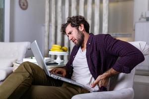 el trabajador independiente cansado que se estira en el sofá sufre de estar sentado mucho tiempo en una postura incorrecta, el empleado masculino tiene dolor de espalda o espasmo espinal trabajando en una posición incómoda. concepto de vida sedentaria foto