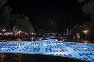 Pasarela sobre piscina iluminada por la noche en complejo turístico foto