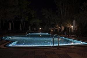 Parasols and deck chairs arranged by illuminated swimming pool at night photo