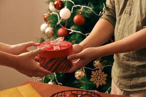 Close-up young asian man holding a christmas red gift box on sofa and christmas tree background at home photo