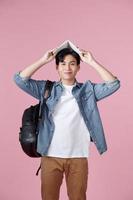 Young male student with open book on his head having fun isolated on a pink background photo