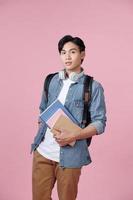 Portrait of smiling young college student with books and backpack against pink background photo