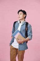 Positive young man with backpack, headphones and notebooks posing on pink background photo