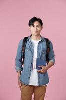 Portrait of smiling young college student with books and backpack against pink background photo