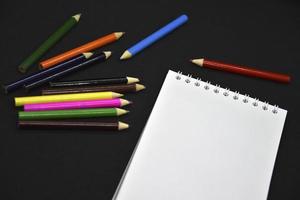 Colored pencils on a black background. Notepad and pencils. photo