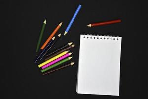 Colored pencils on a black background. Notepad and pencils. photo