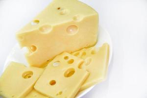 un gran trozo de queso con agujeros en el plato. queso picado y rodajas pequeñas sobre un fondo blanco. Queso natural jugoso y delicioso. agujeros de queso foto