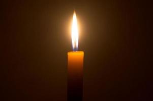 una sola llama de vela encendida o luz que brilla en una vela amarilla aislada en un fondo rojo oscuro en la mesa de la iglesia para navidad, funeral o memorial foto