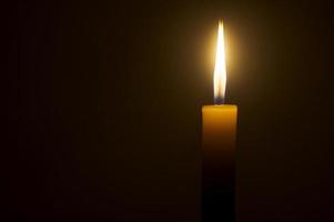 una sola llama de vela encendida o una luz que brilla en una vela amarilla aislada en un fondo rojo u oscuro en la mesa de la iglesia para Navidad, funeral o servicio conmemorativo foto