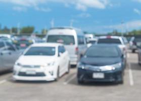 blurred photo of cars parking in open area or outdoor parking lot is taken in front of office, university, school, department store or hospital with blue sky