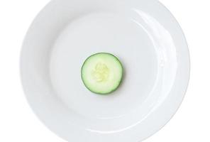 Top view of single fresh cucumber slice on white plate isolated on white background photo