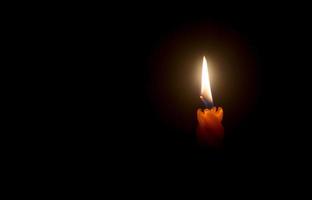 una sola llama de vela encendida o luz que brilla en una hermosa vela espiral naranja sobre fondo negro u oscuro en la mesa de la iglesia para navidad, funeral o memorial foto