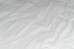 White crumpled or wrinkled bedding sheet or blanket with pattern after guest's use taken in hotel, resort room with copy space, Untidy blanket background texture photo