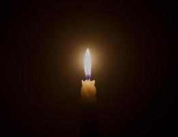 una sola llama de vela encendida o luz que brilla en una vela blanca en espiral sobre fondo negro u oscuro en la mesa de la iglesia para Navidad, funeral o servicio conmemorativo foto