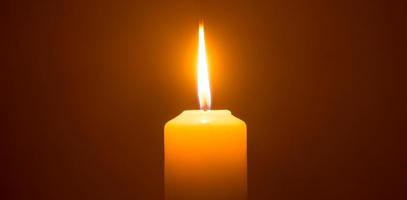 una sola llama de vela encendida o luz que brilla en una gran vela amarilla aislada en un fondo rojo u oscuro en la mesa de la iglesia para Navidad, funeral o servicio conmemorativo