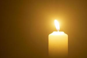 foto borrosa de una sola llama de vela encendida o luz que brilla en una vela amarilla sobre fondo de color naranja o rojo en la mesa de la iglesia para Navidad, funeral o servicio conmemorativo