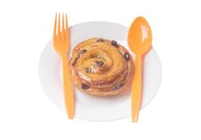 Spiral danish pastry with raisin on top on white plate with plastic spoon and fork served for breakfast isolated on white background photo