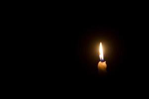 A single burning candle flame or light glowing on a spiral white candle on black or dark background on table in church for Christmas, funeral or memorial service photo