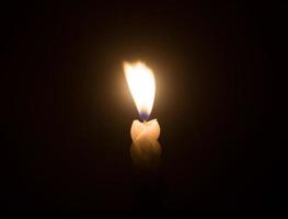 A single burning candle flame or light glowing on a spiral white candle against little blowing wind on black or dark background on table in church for Christmas, funeral or memorial service photo