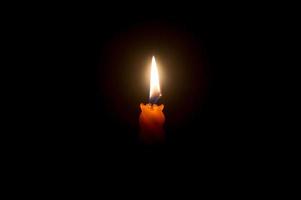 una sola llama de vela encendida o luz que brilla en una hermosa vela espiral naranja sobre fondo negro u oscuro en la mesa de la iglesia para Navidad, funeral o servicio conmemorativo