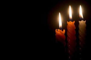 tres llamas de velas encendidas o luces que brillan en velas espirales blancas y naranjas sobre fondo negro u oscuro en la mesa de la iglesia para navidad, funeral o servicio conmemorativo foto