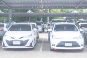 blurred photo of cars parking in open area or outdoor parking lot with roof is taken in front of office, university, school, department store or hospital